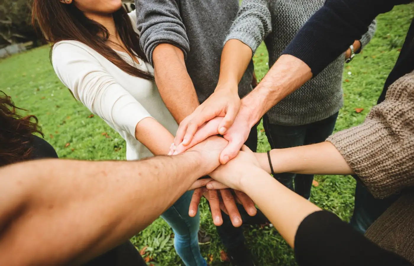Groupe de personnes posant leurs mains ensemble, symbolisant la collaboration et la solidarité au sein d’une communauté.