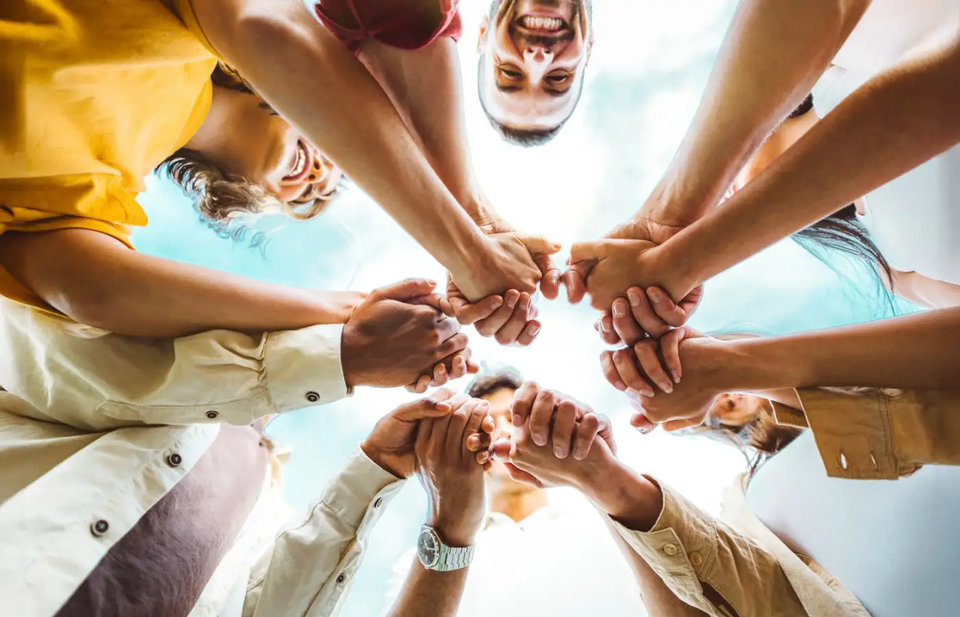 Groupe de personnes se tenant les mains en cercle, vu de dessous, symbolisant la collaboration et l'unité dans la construction d'une communauté.