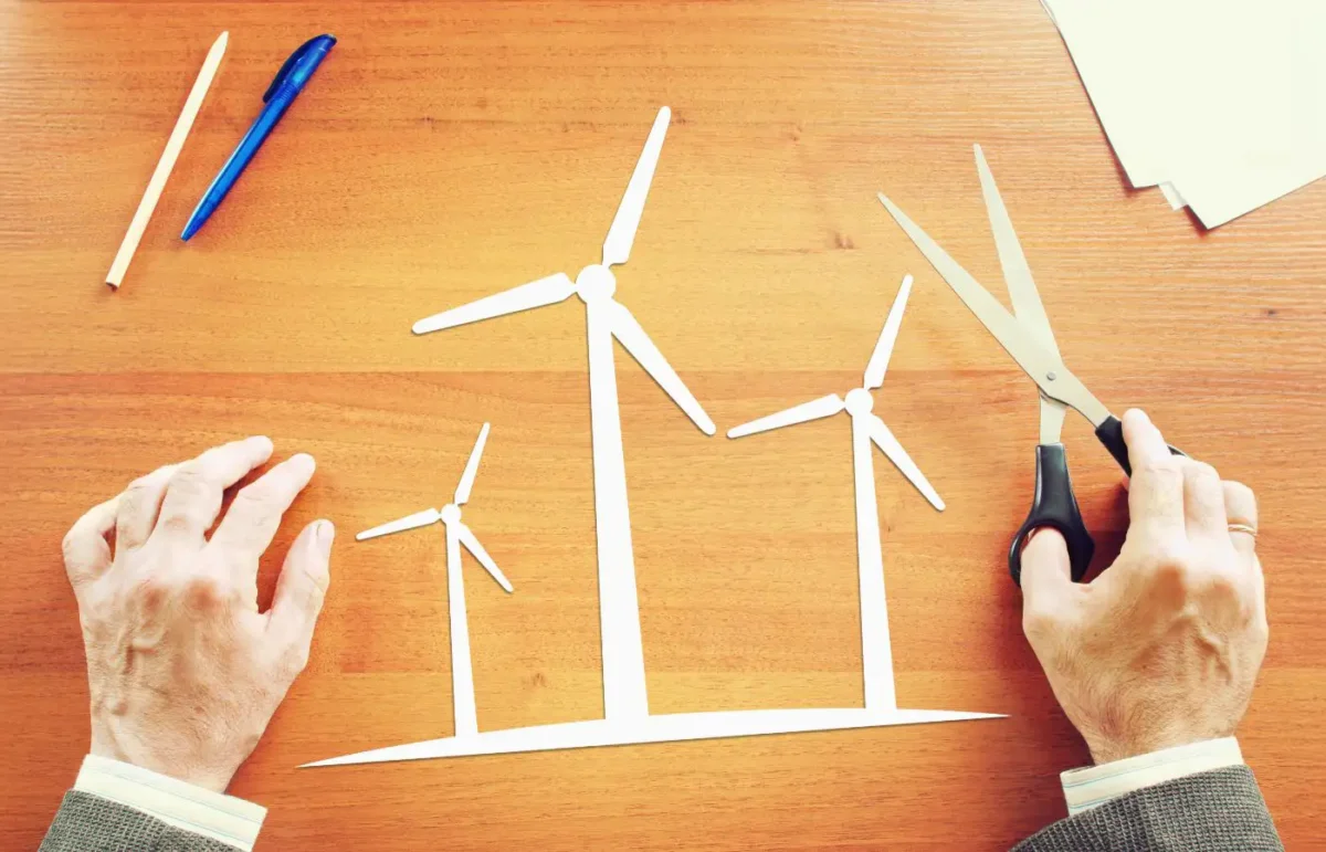 Personnes créant des éoliennes en papier sur un bureau en bois avec des ciseaux et des stylos, symbolisant la planification et la conception de projets d'énergie renouvelable.
