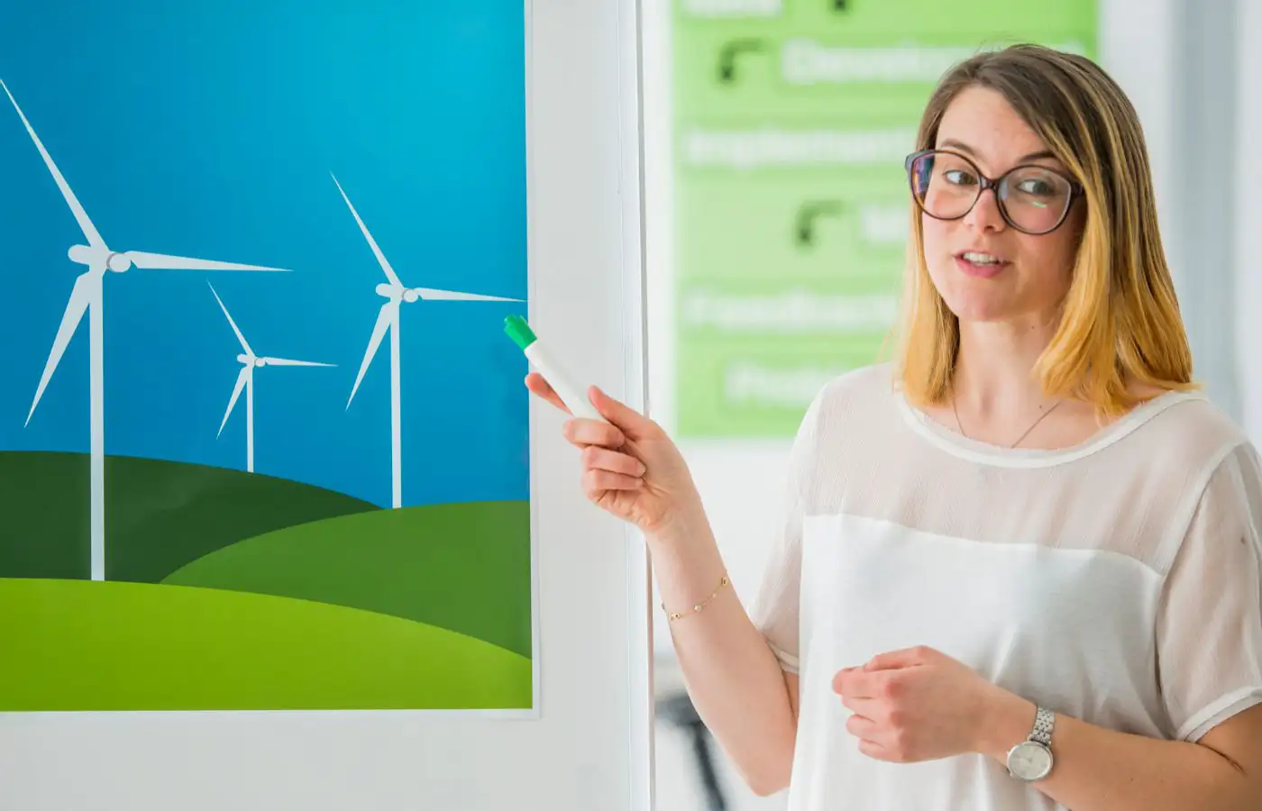 Femme expliquant le concept des éoliennes lors d'une présentation, symbolisant la sensibilisation et l'éducation au partage d'énergie et aux énergies renouvelables.
